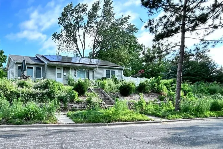A ranch house on a corner lot above a planted slope with a stone wall and steps